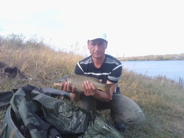 Рыболов с пойманным карпом на берегу водоема во время рыбалки