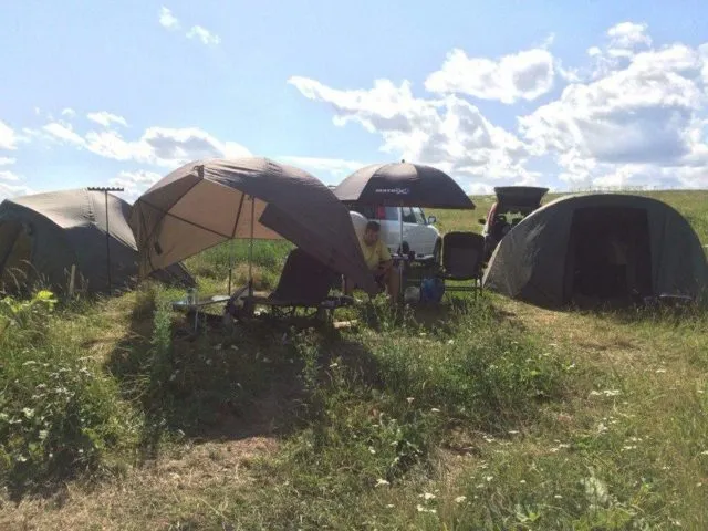 Лагерь карпятников с палатками и зонтами на берегу водоема для ловли карпа