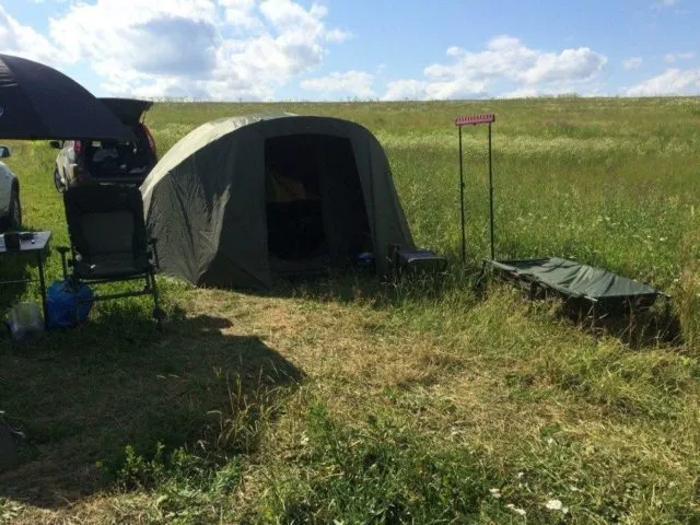 Палатка для карпфишинга с раскладушкой и род-подом на берегу водоема летом