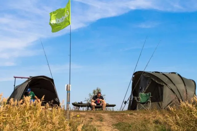 Карповый лагерь с палатками, удилищами и флагом на берегу водоема для ловли карпа
