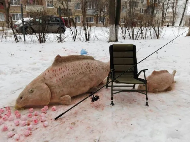 Снежная скульптура гигантского карпа с креслом и удочкой для карпфишинга