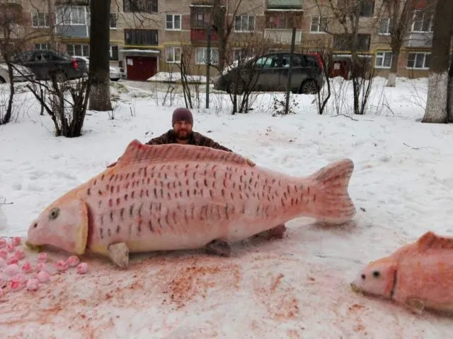 Рыбак с гигантским карпом из снега во дворе жилого дома зимой